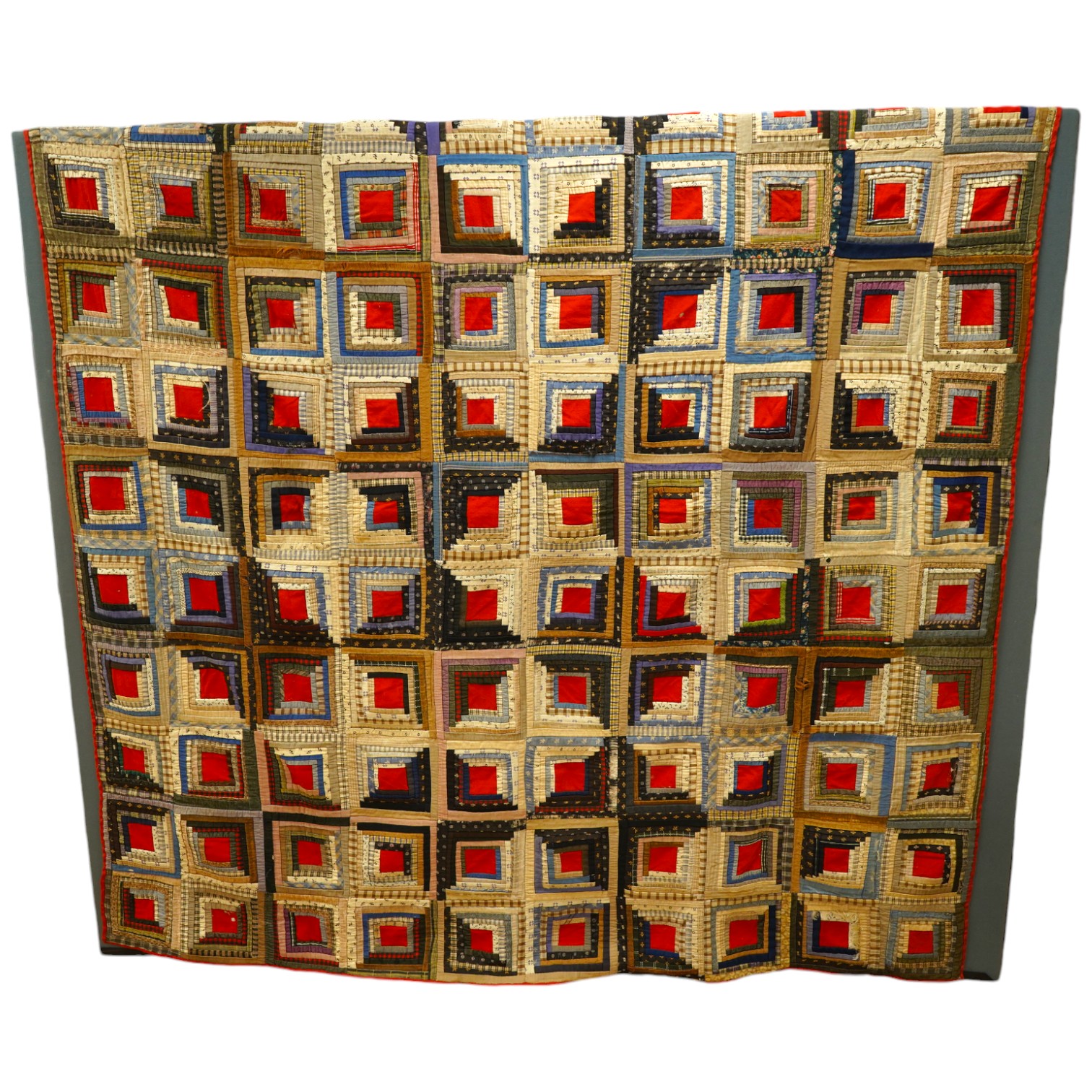 An early 20th century American ‘Log Cabin’ quilt, with a simple same coloured squared patchwork under side, the ‘Log Cabin’ worked in narrow bands of multi patterned and coloured strips of fabric into squares with a plai